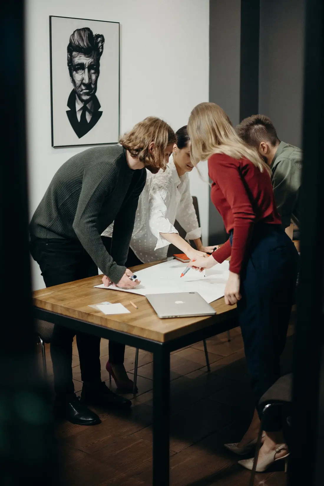 Four colleagues standing around a table reviewing printed layouts and a laptop