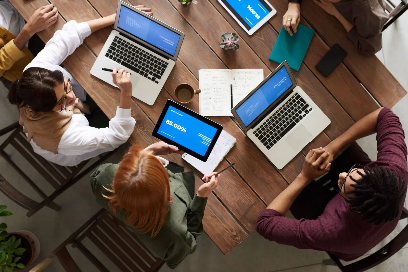 Overhead view of colleagues working on laptops and tablets around a wooden table